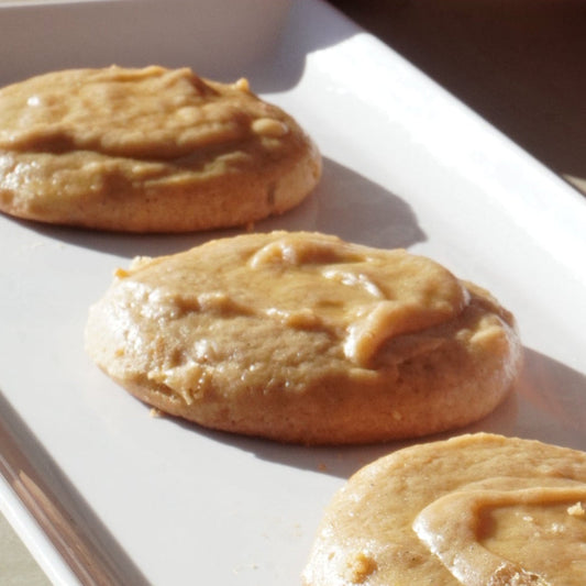 Three eggnog cookies on a white plate with pumpkins in the background
