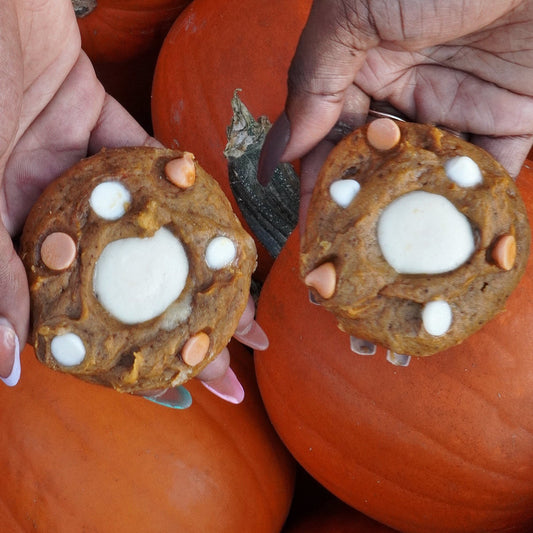 Two hands holding cookies with candle-like centers in front of pumpkins